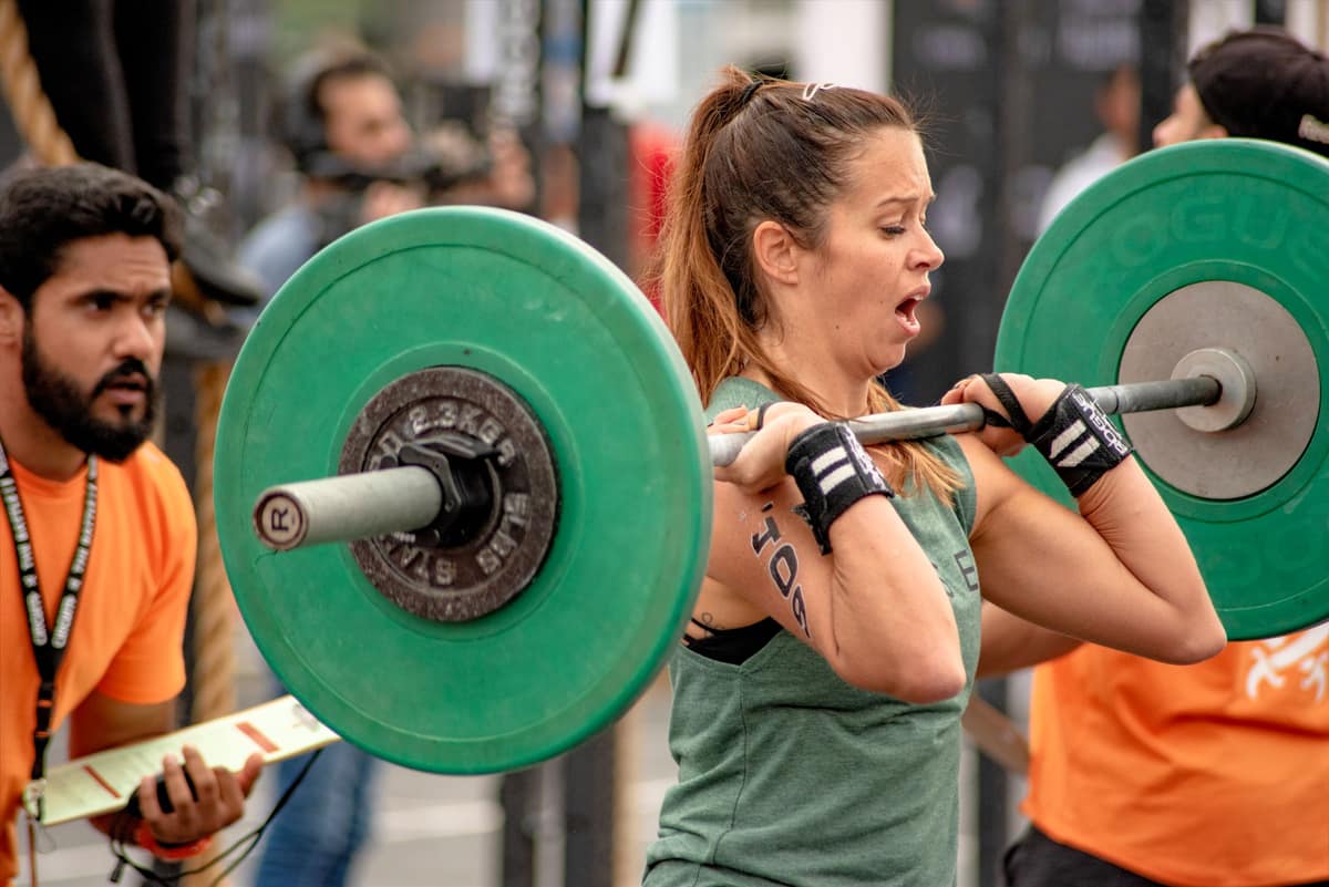 A woman lifting a barbell with green plates while friends look on